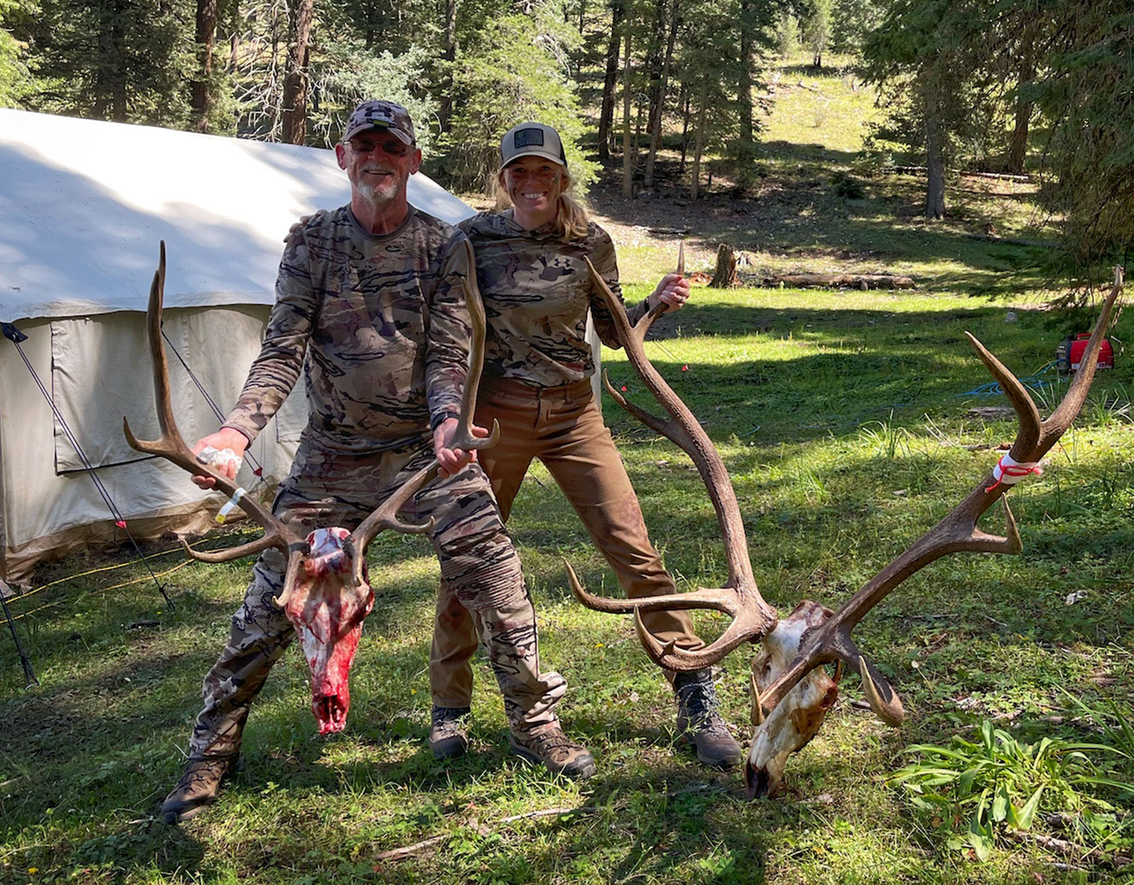 A male and female hunter pose for a photo at camp with the two elk skulls from the bulls they harvested.