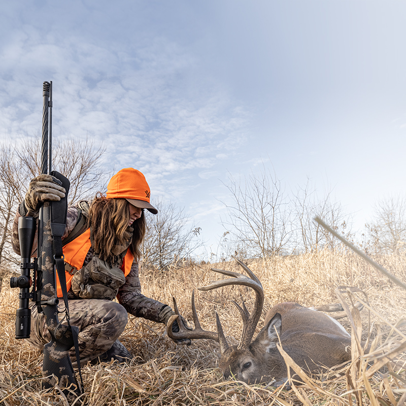 a female hunter with a rifle and a downed deer