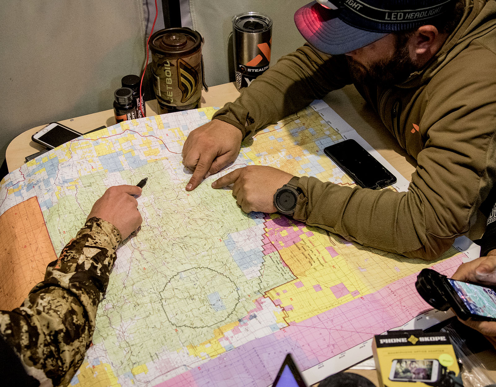 Two people point to areas on a print map, seated around a table.