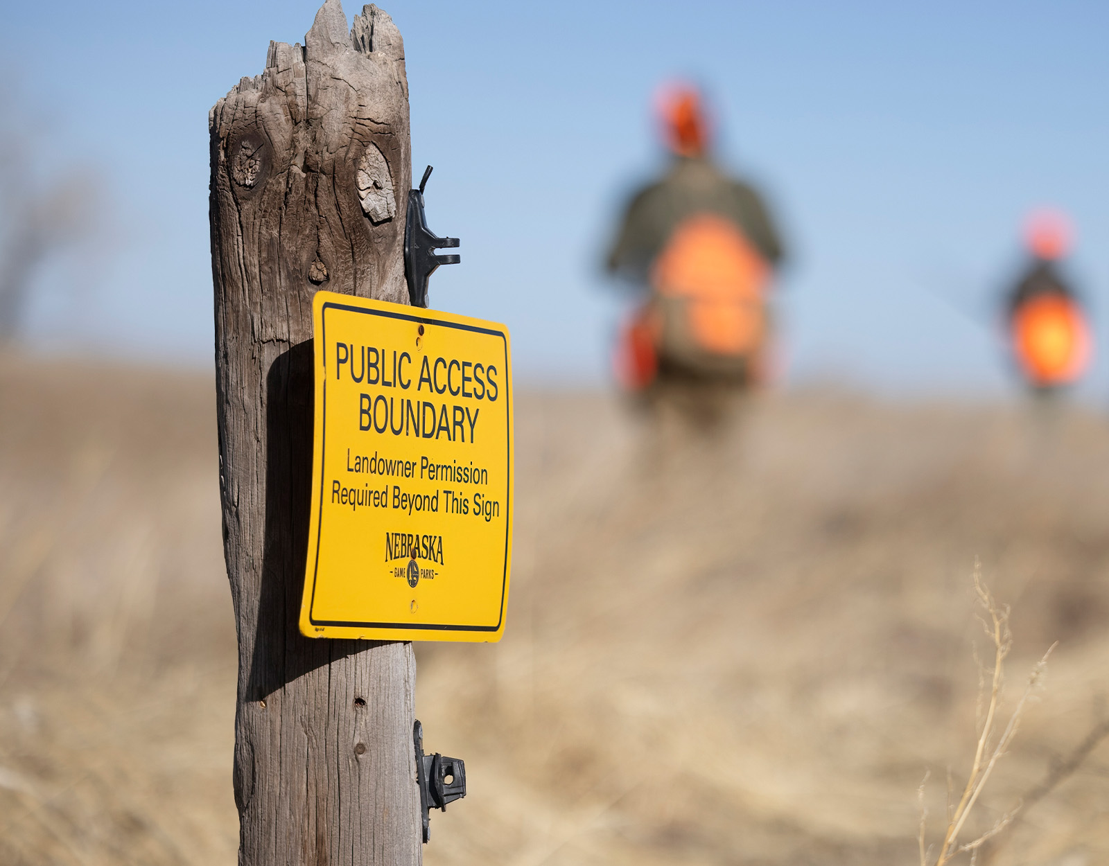 A public access sign on a fence post with hunters in the background.