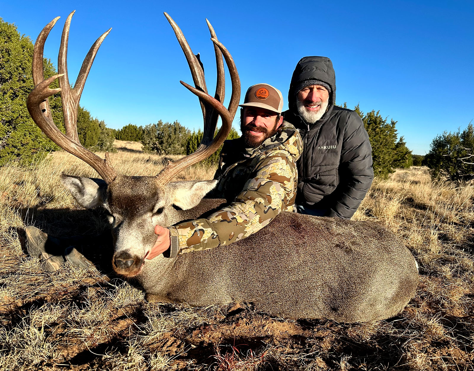 Two men pose with the mule deer buck one of them harvested.