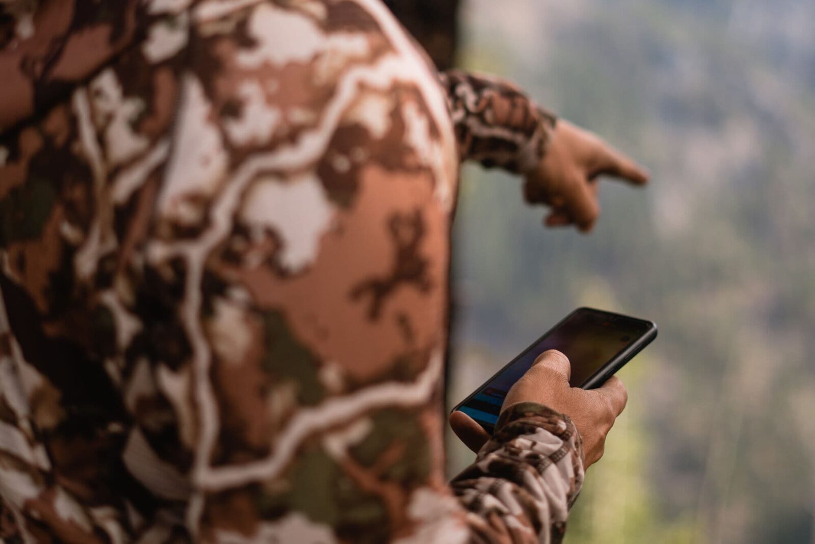 A hunter uses his mobile phone in the field and points at something in the distance. 