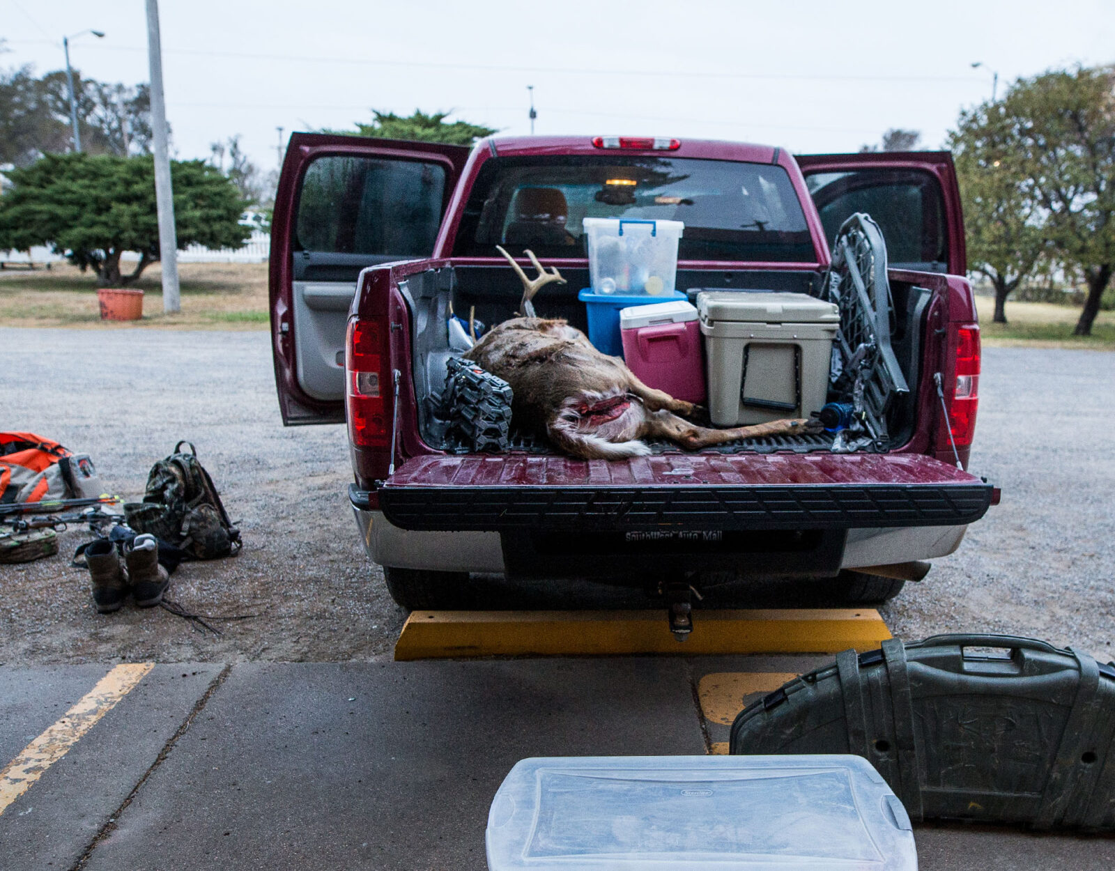 A harvested deer in the bed of a truck along with hunting gear.