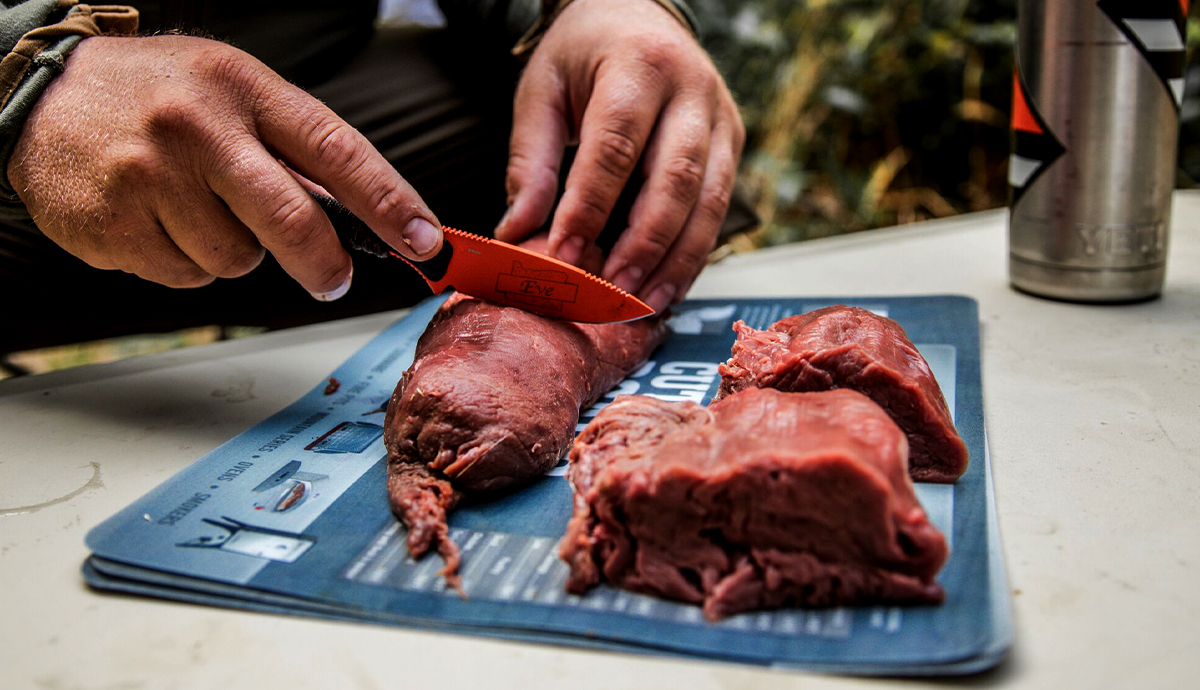 A person cuts meat on a cutting board.