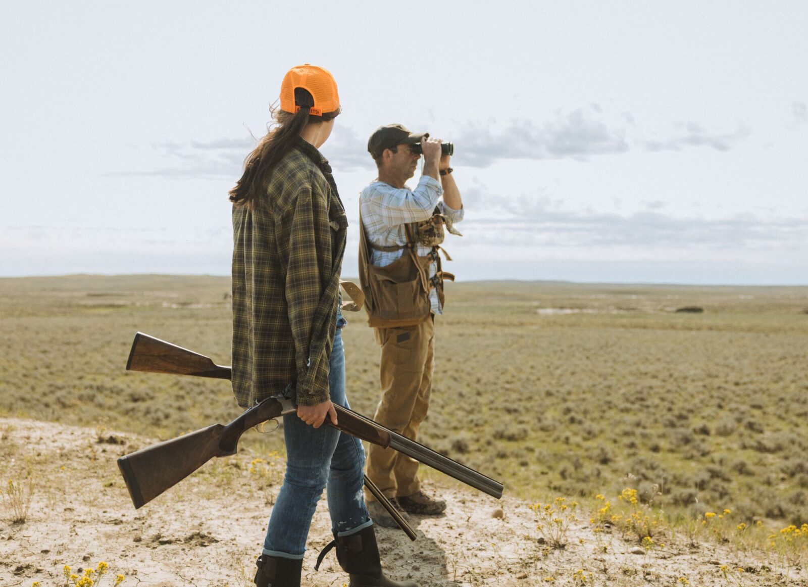 Two upland hunters in the field, one using binoculars.