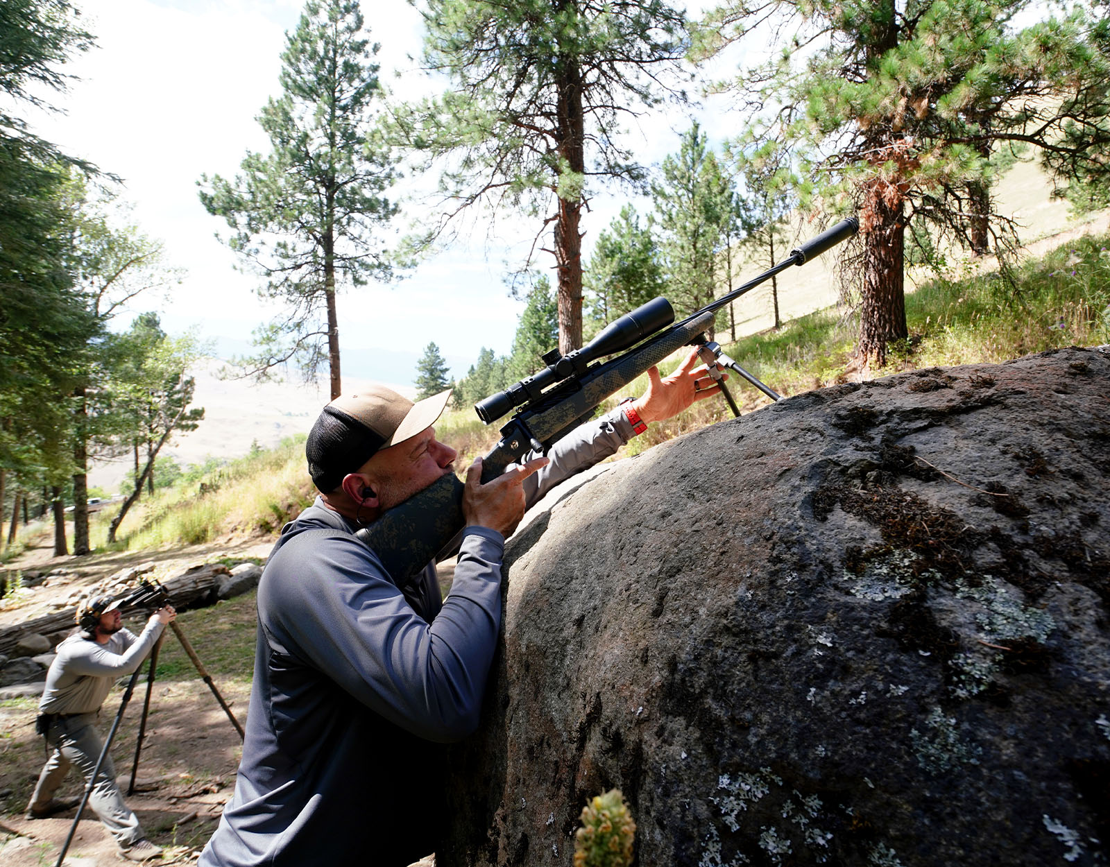 A man uses a rock as tripod for his rifle.