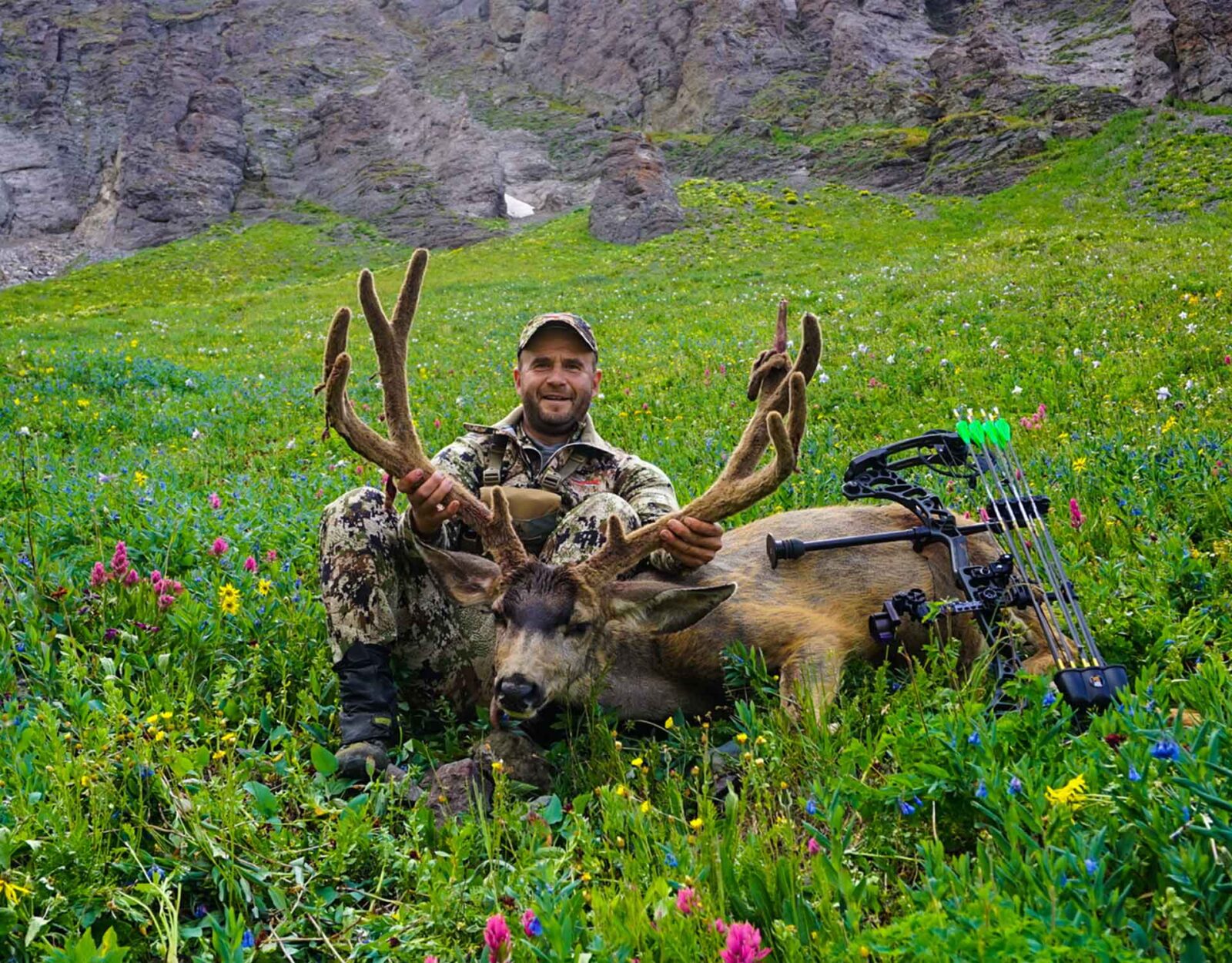 A man poses with the mule deer buck he harvested.