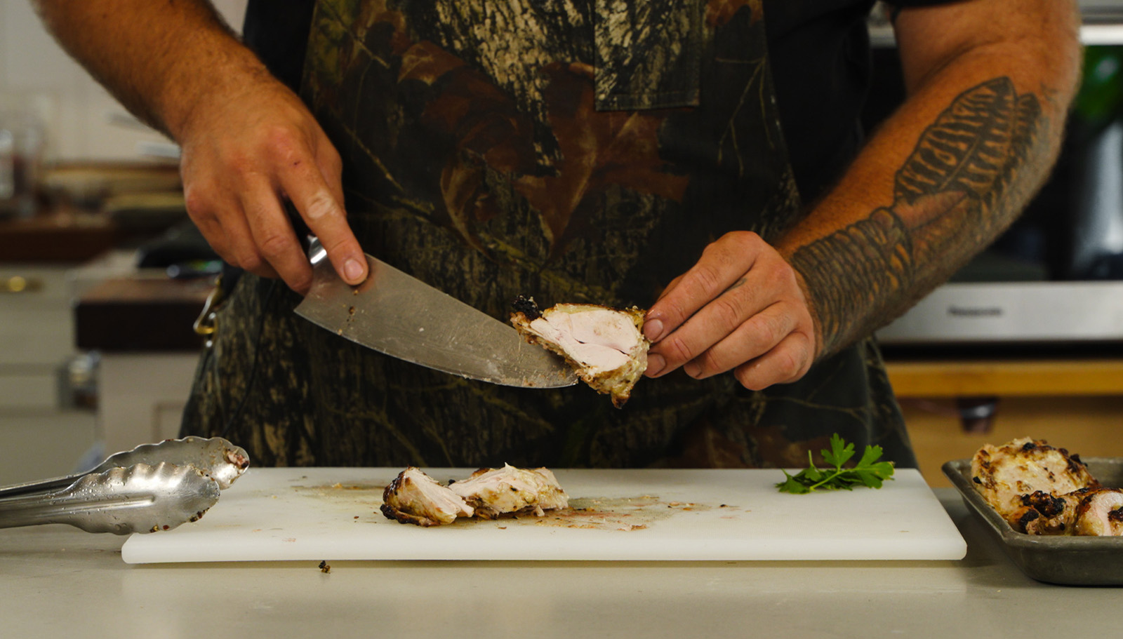A man cuts up grilled pheasant using a kitchen knife.
