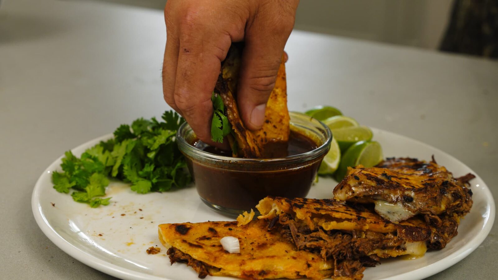 A hand dunks a taco into dipping sauce.