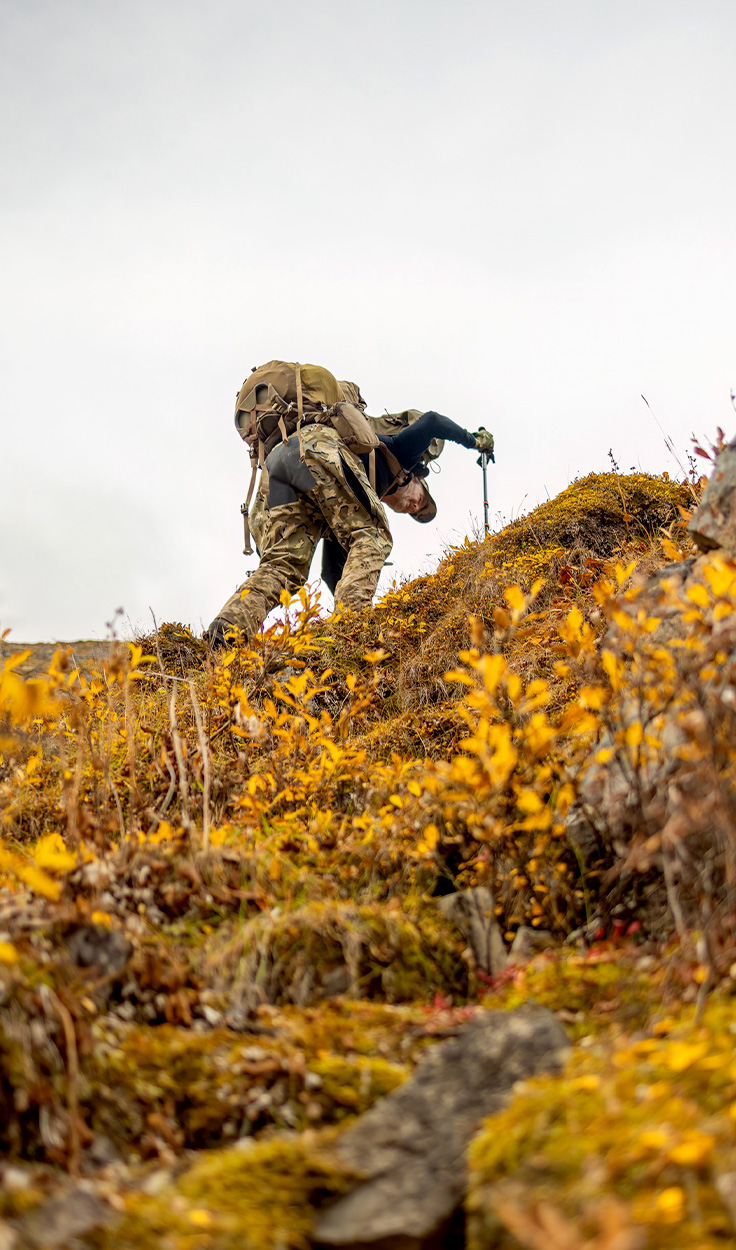 A hunter trekking up a steep hill.