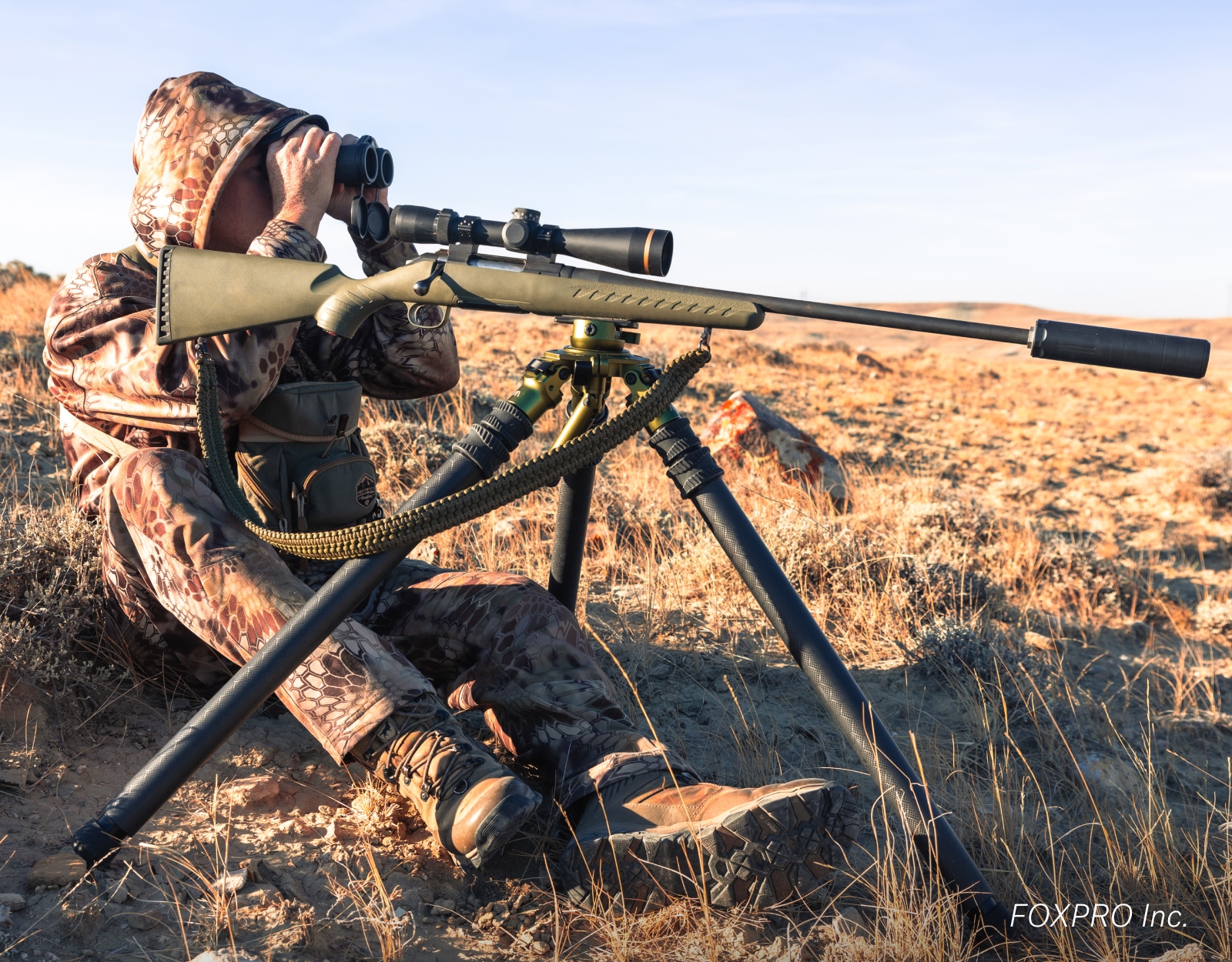 A hunter glasses behind a rifle.