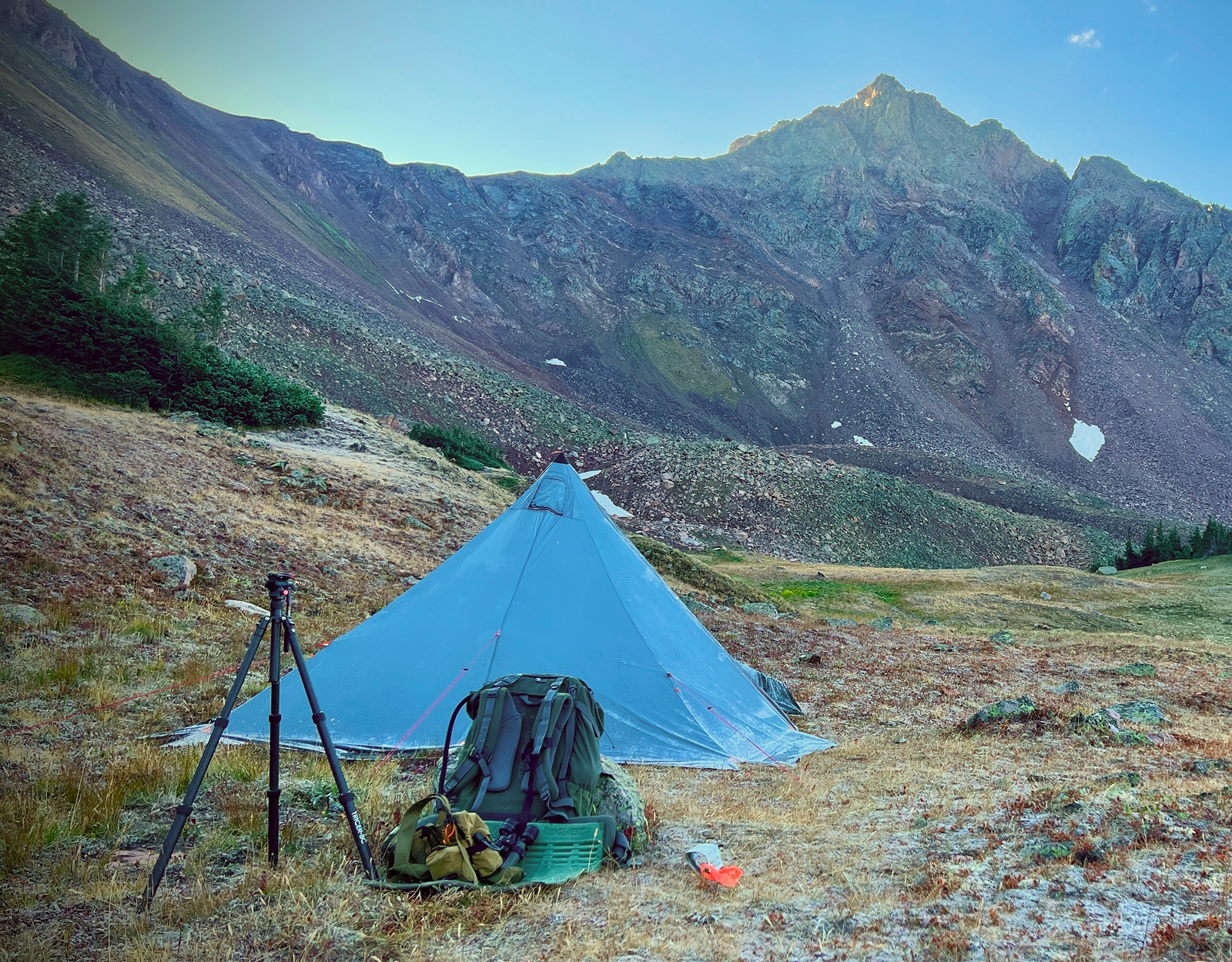A tipi tent and tripod stand pitched in remote mountainous backcountry.