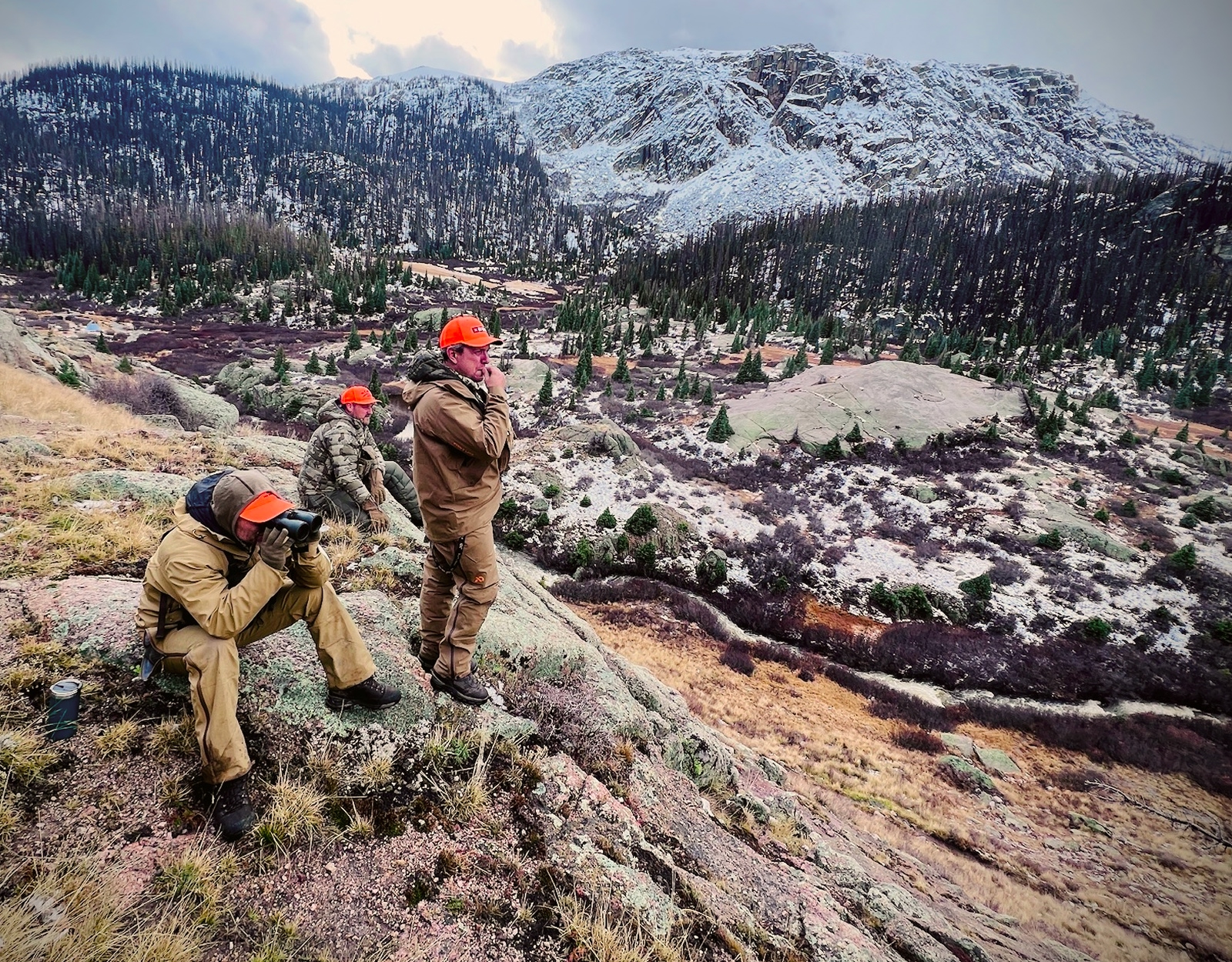 Hunters stand on a glassing knob and use binoculars to explore the land.