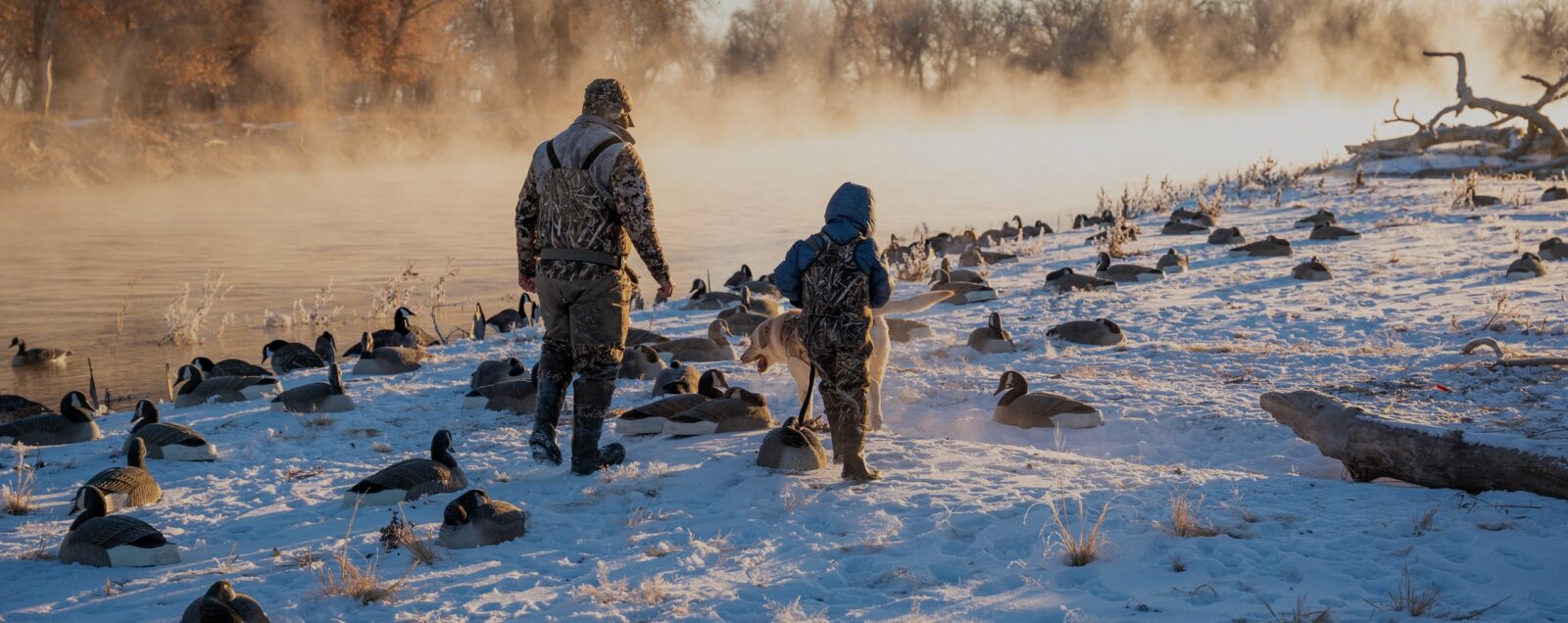 Two hunters walk in a snow field.