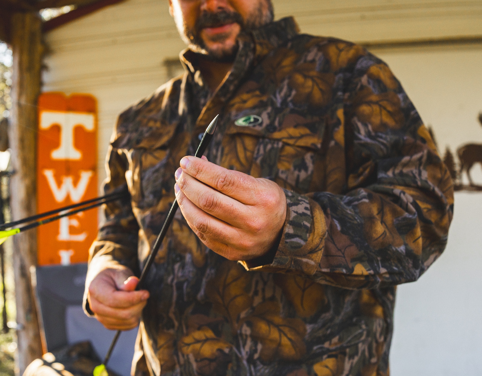 A man in camo holds an arrow with a field tip on it.