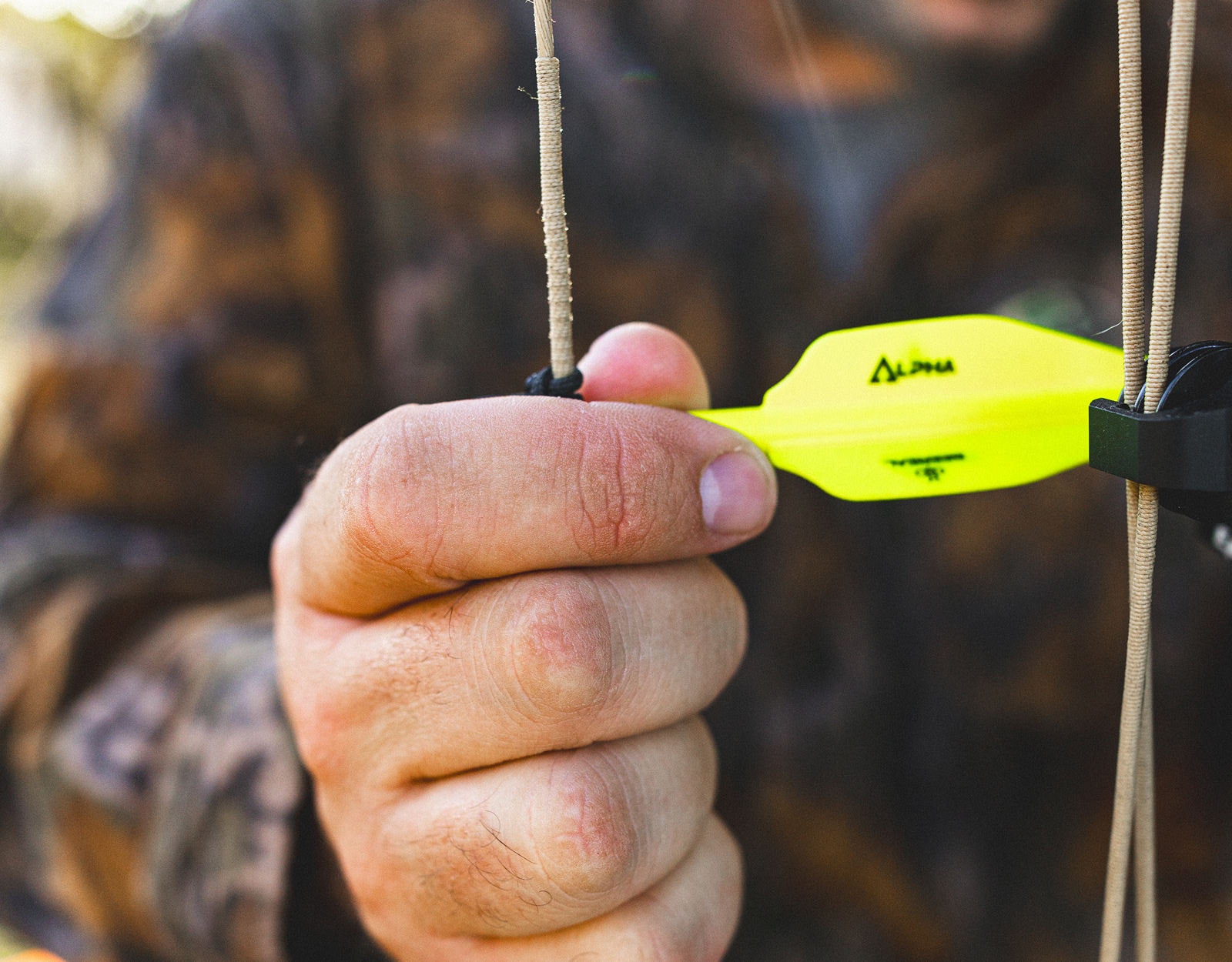 A man's hand holds an arrow with yellow fletching.