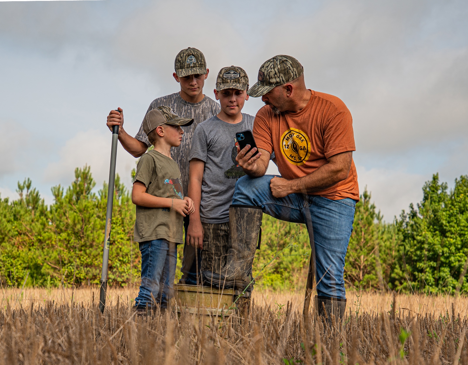 A father and his son stand in a field, and the father shows the son something on his mobile device.