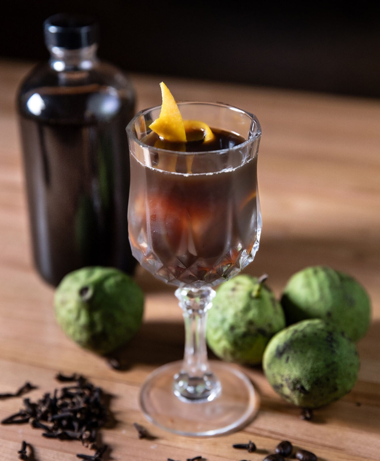 A Nocino Manhattan poured into a cocktail glass with green walnuts on the table