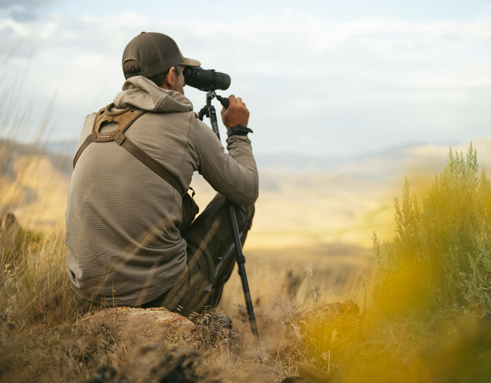 A hunter uses binoculars on a tripod.