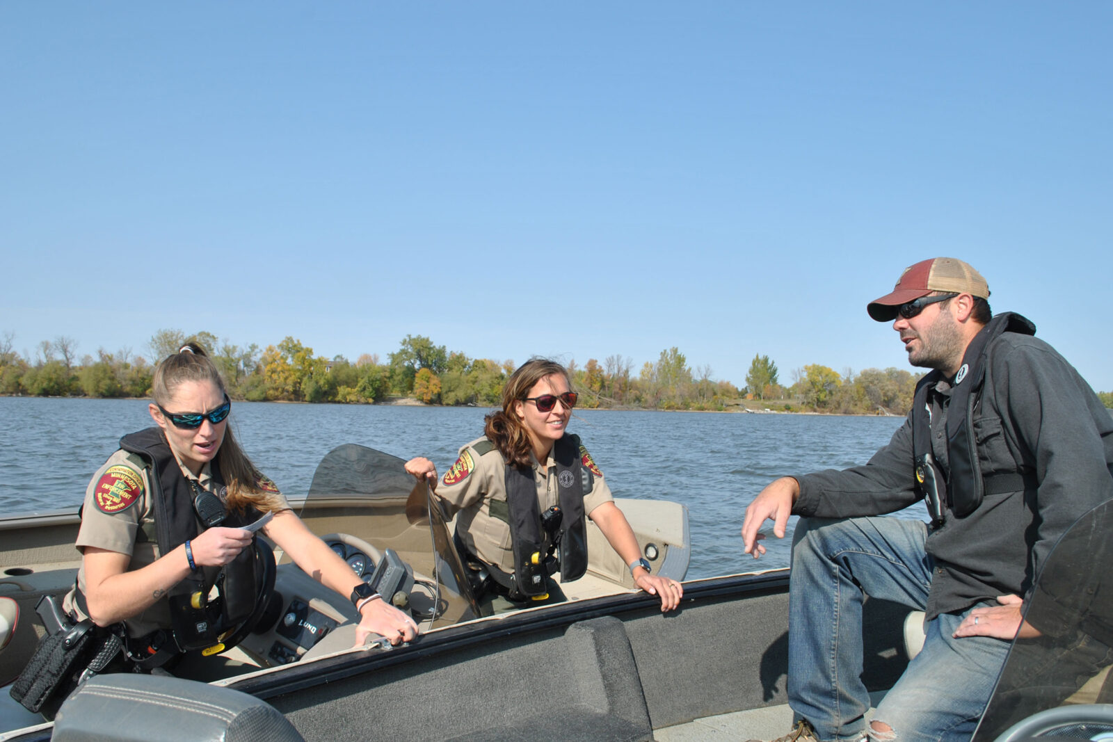 Two female officials check a fisherman's licenses, pulling their boat up next to his. 