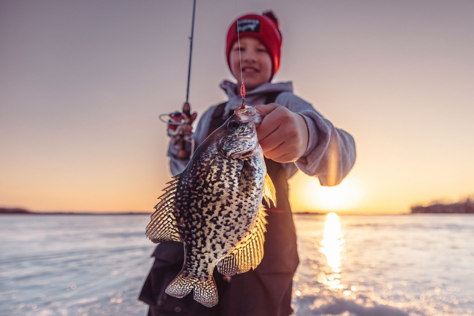 A child holds the fish they caught up to the camera.