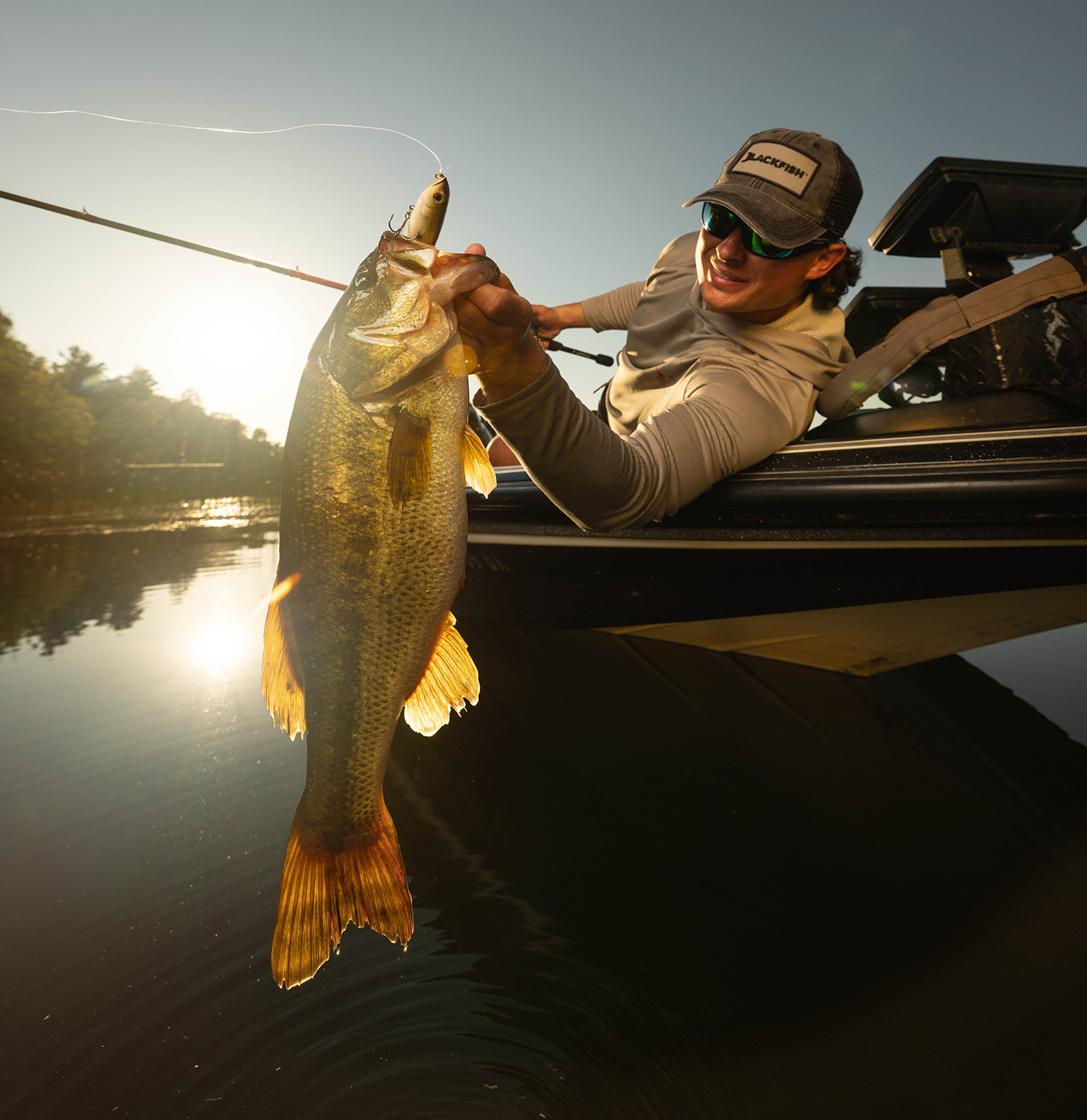An angler holds a largemouth bass off the side of a boat.