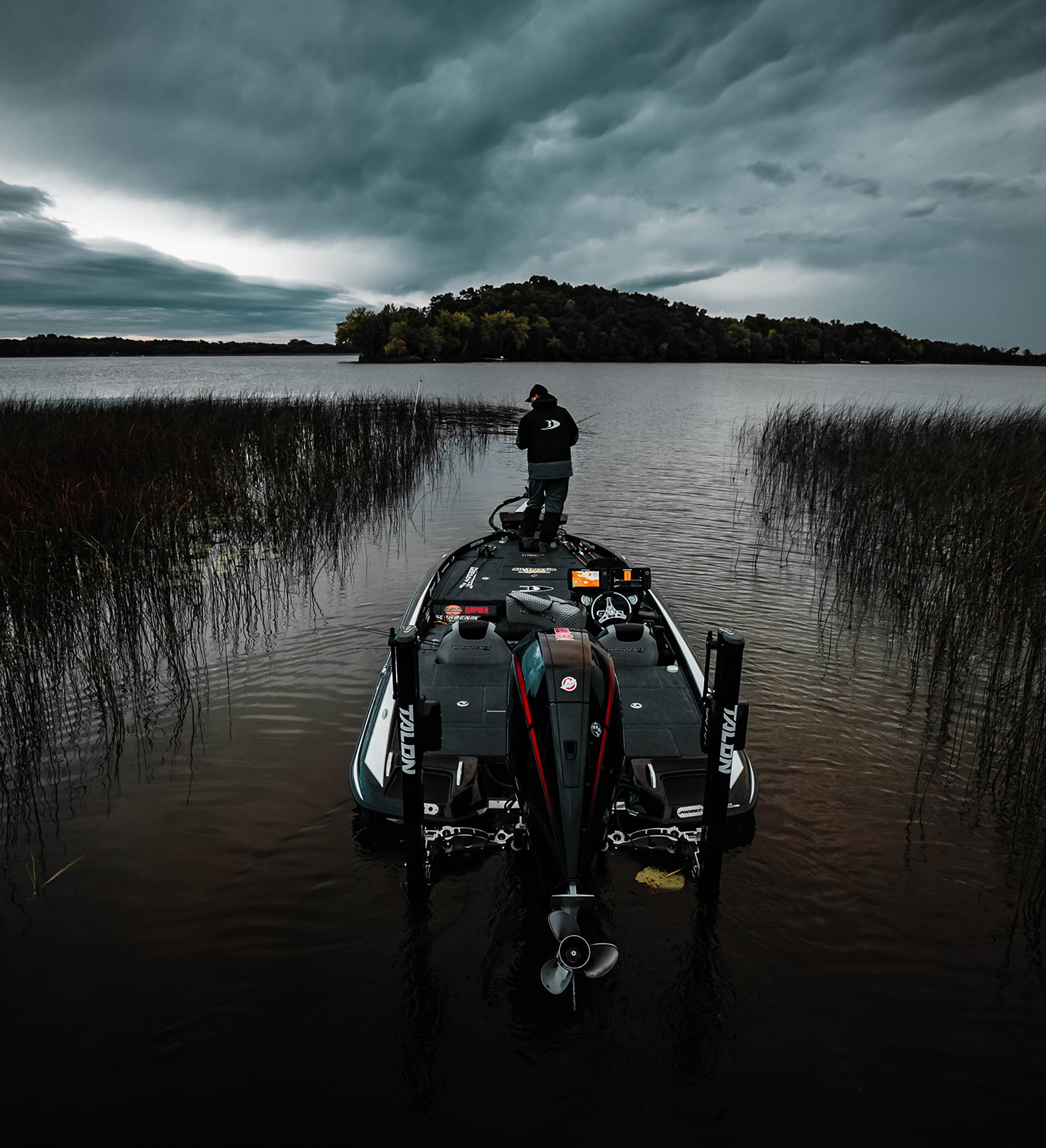 A fisherman in a bass boat on a weedy lake.