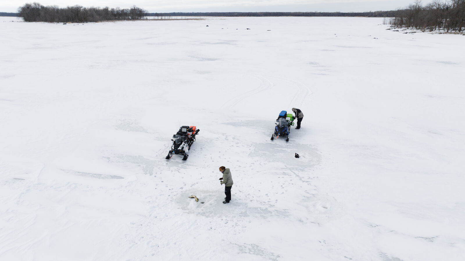 Ice fisherman on a frozen lake with their snowmobiles and gear handy. 