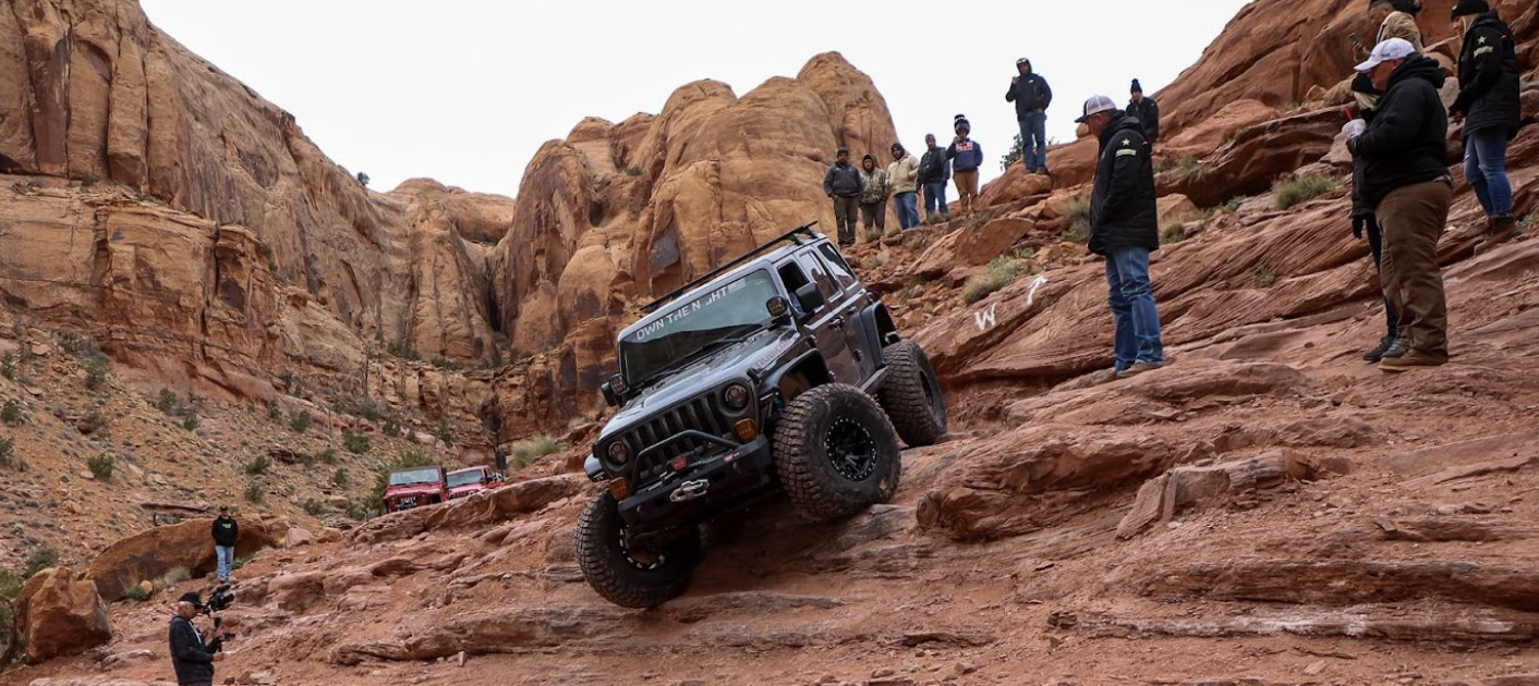 off-raoders standing around a jeep crawling down a rock