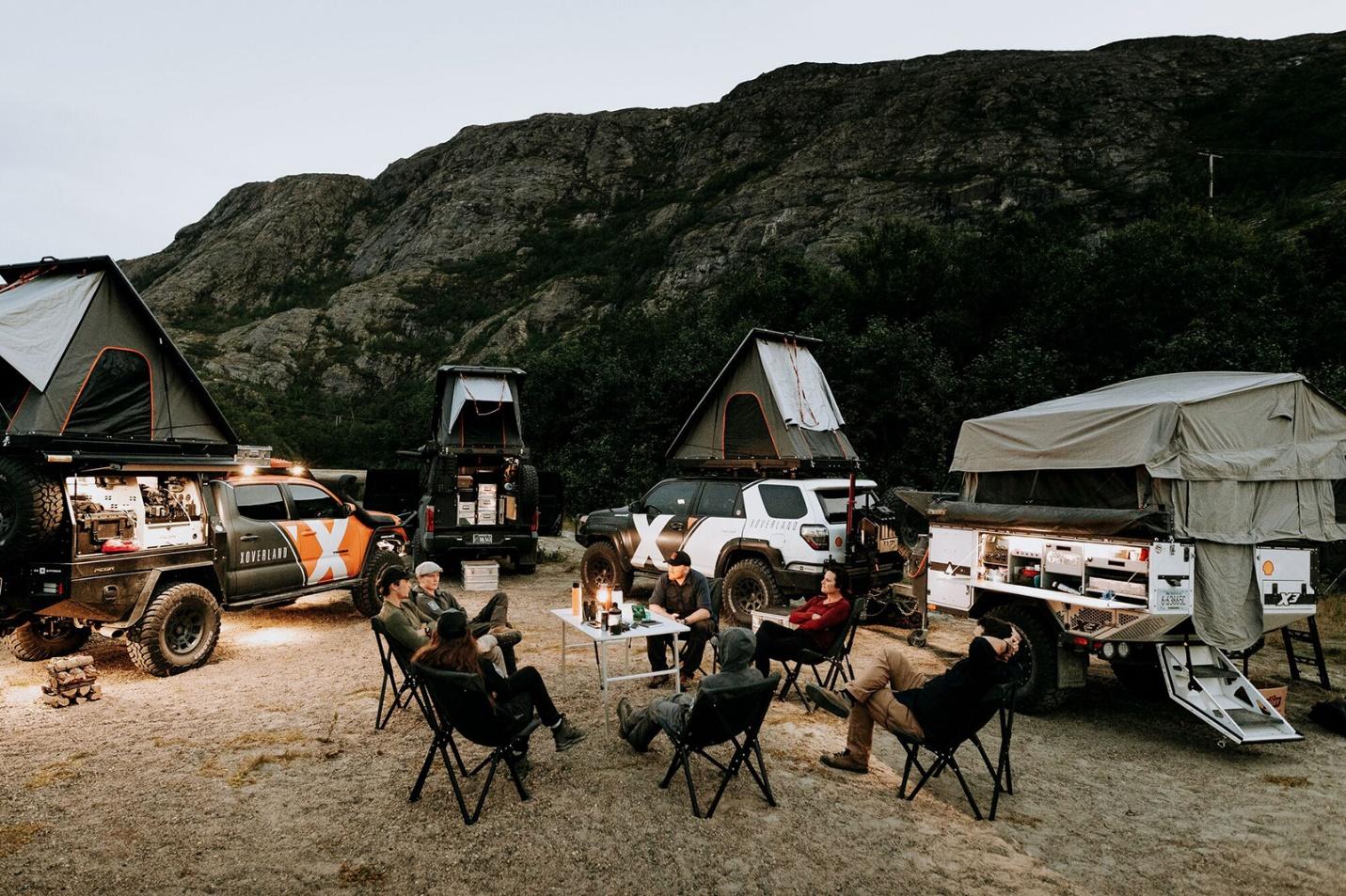 People sitting in chairs outside with off-road tents and campers in the background